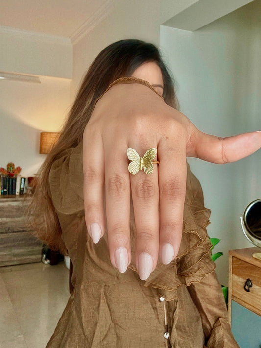 A person showing a gold-colored butterfly ring on their finger.