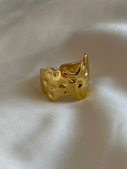 A gold-colored ring with a textured surface laying on a white silky fabric.