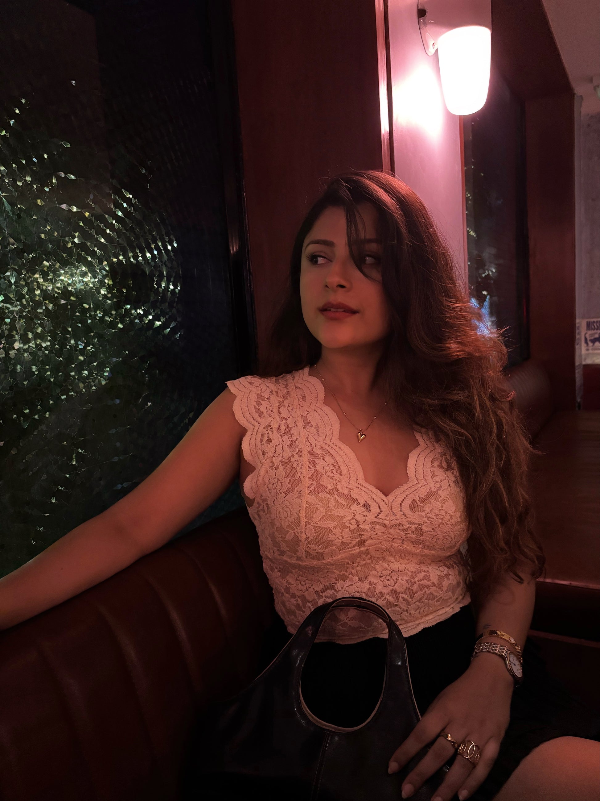 Woman sitting indoors with a blurred background wearing a gold heart necklace