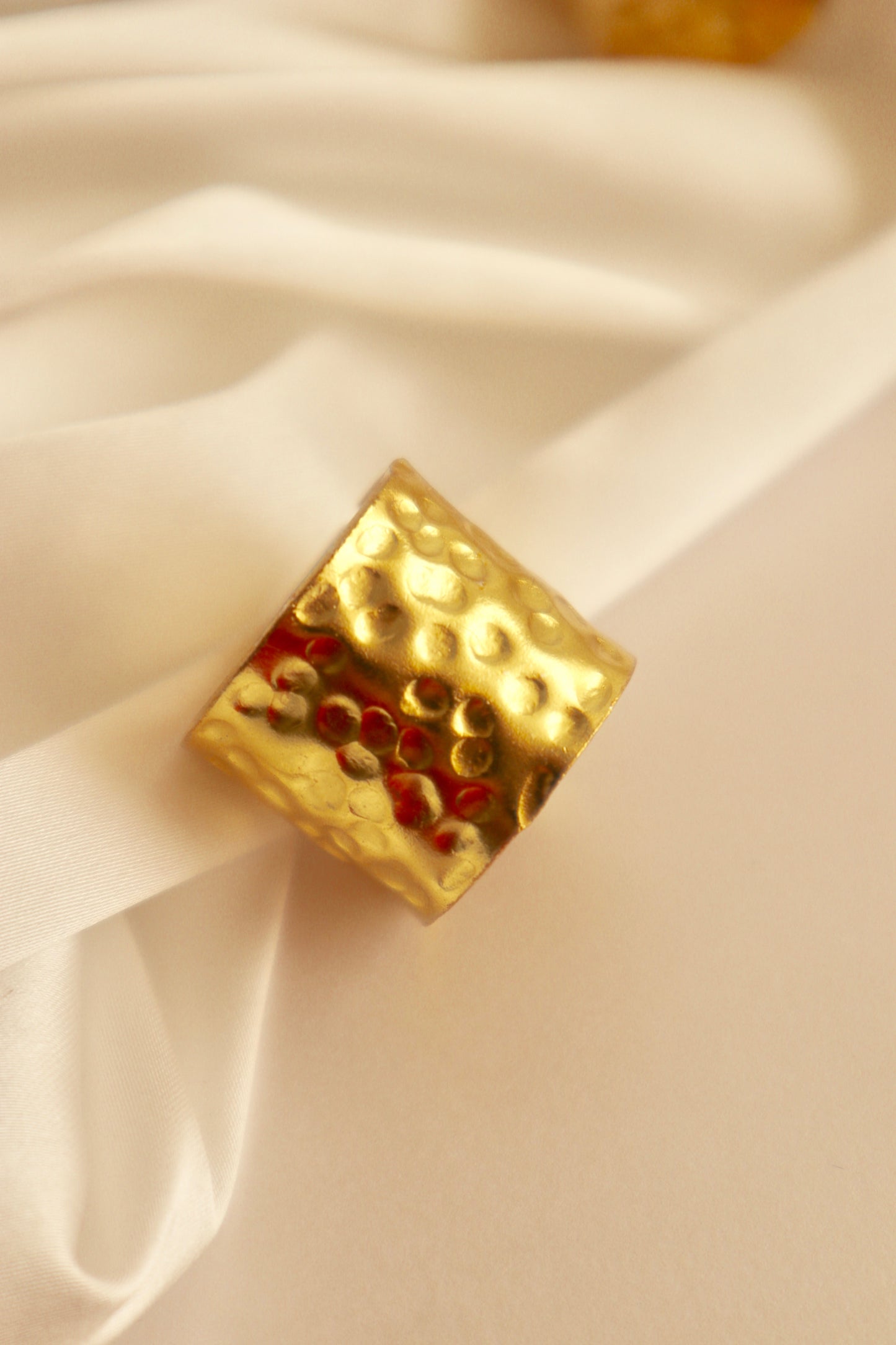 A gold-colored chunky ring with a hammered design, displayed on a white fabric surface.