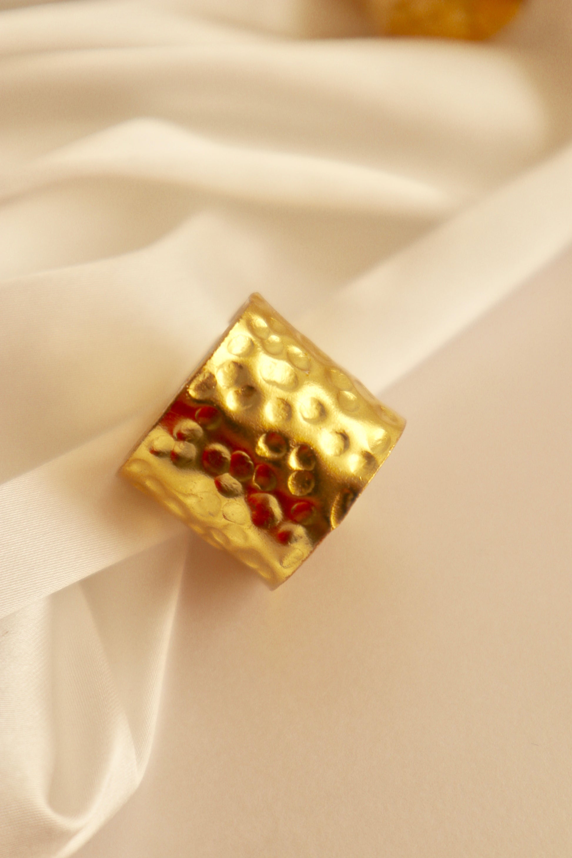 A gold-colored chunky ring with a hammered design, displayed on a white fabric surface.
