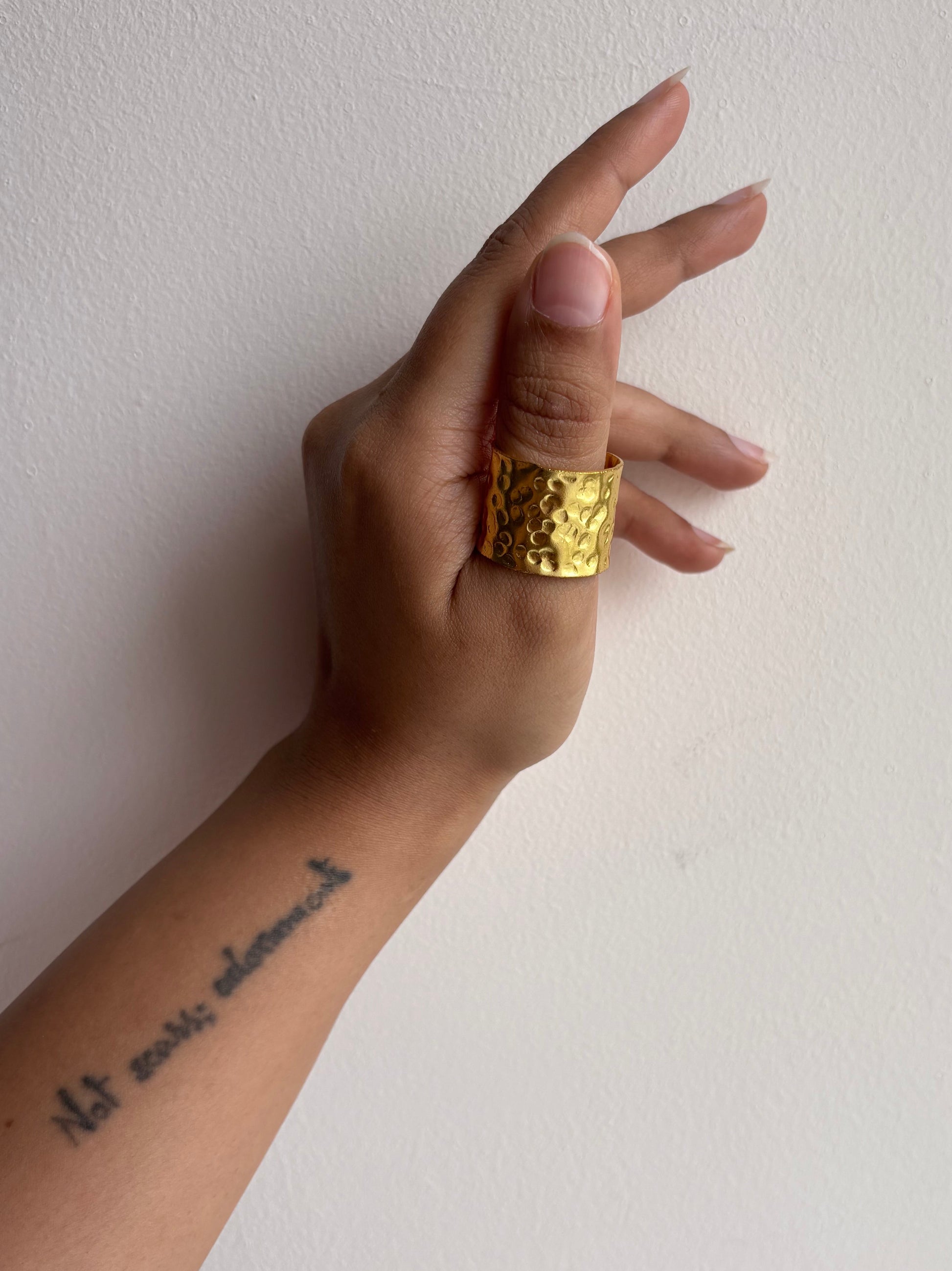 Hand wearing a gold ring on a plain background