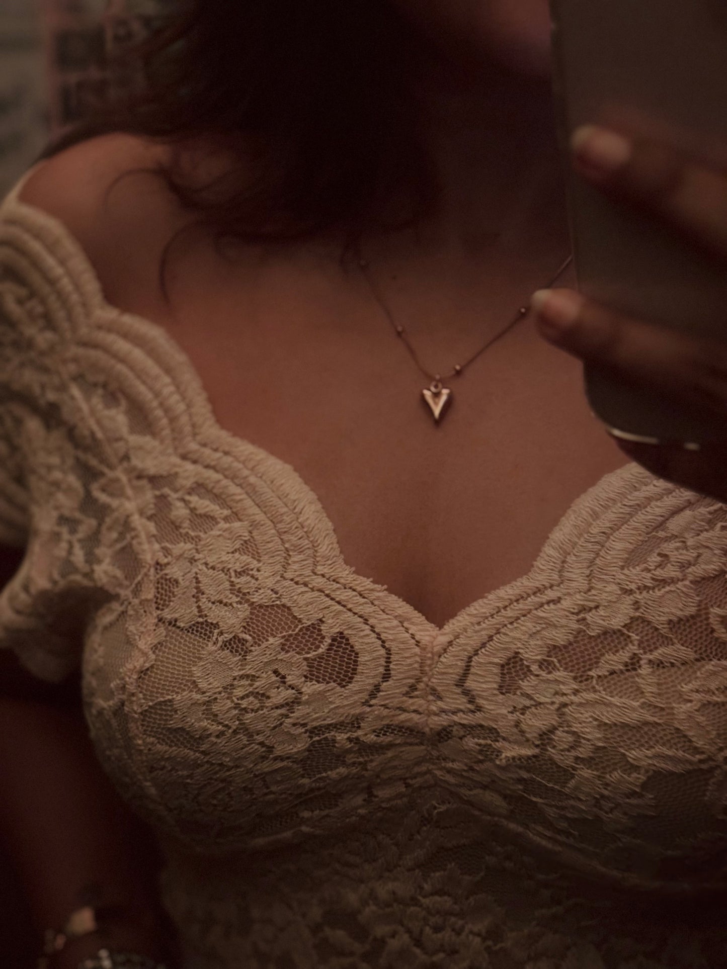 Person wearing a lace garment and gold necklace with a heart pendant.