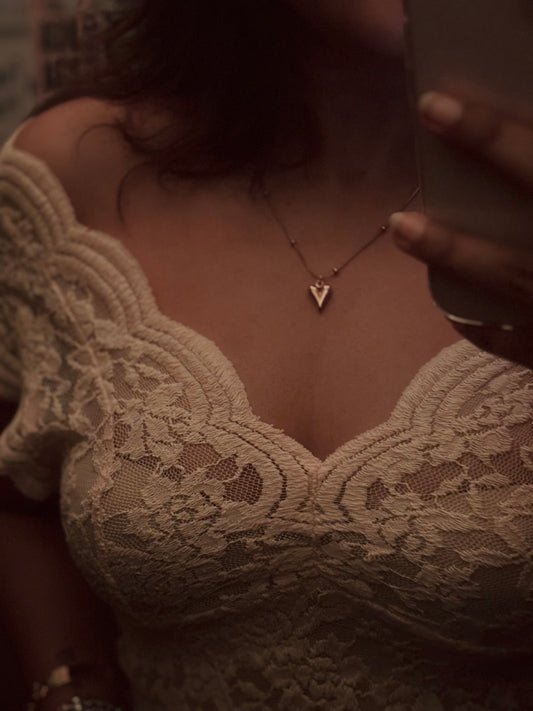 Person wearing a lace garment and gold necklace with a heart pendant.