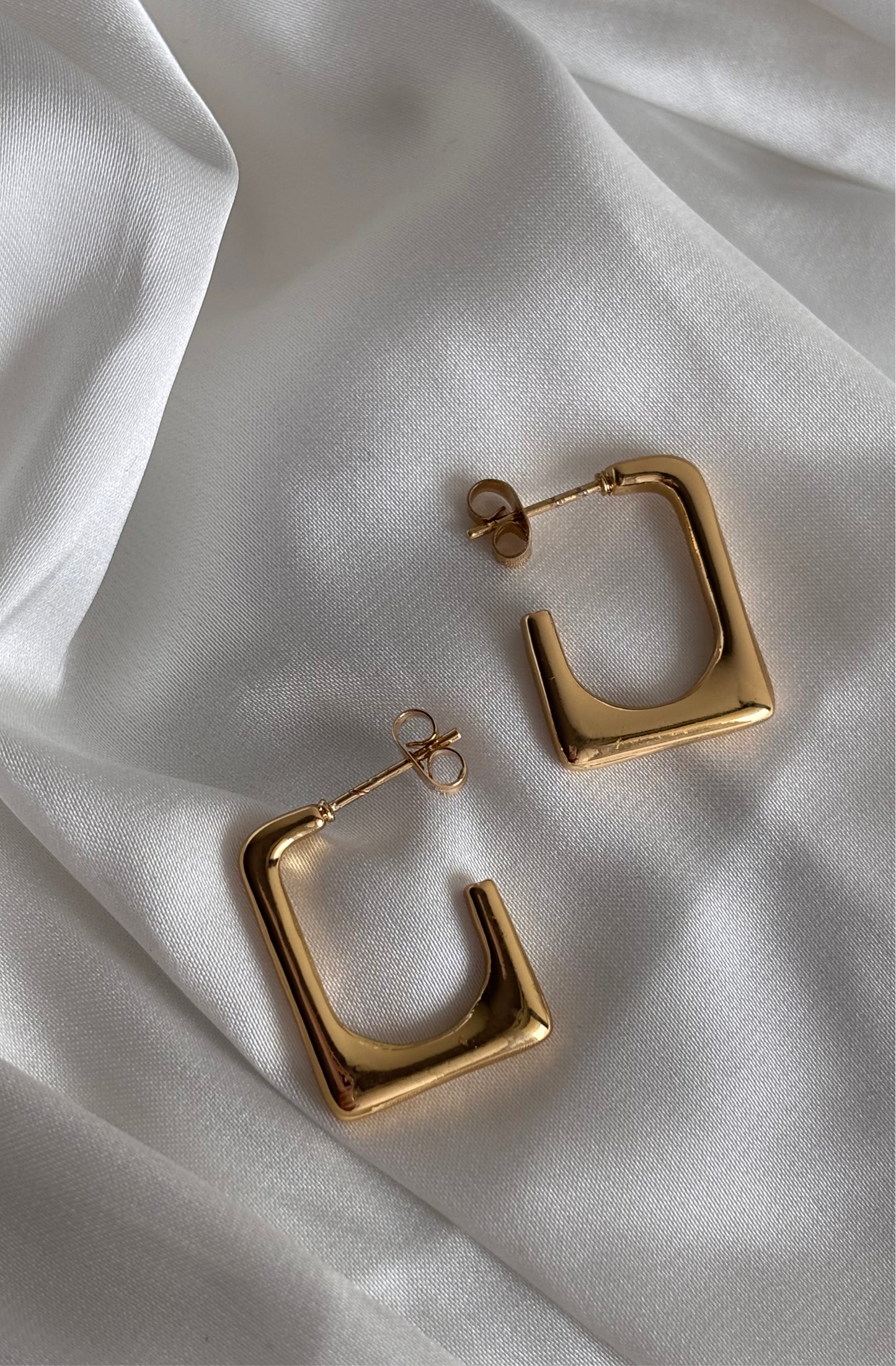 Gold hoop earrings on a white fabric background